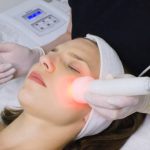 beautician doing red led light therapy to female customer in beauty salon, facial photo therapy for skin pore cleansing. Anti-aging treatments and photo rejuvenation procedure